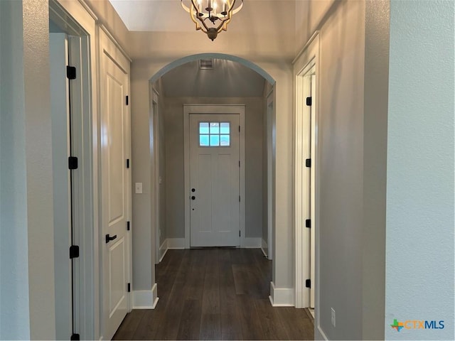 doorway featuring dark wood finished floors, arched walkways, an inviting chandelier, and baseboards
