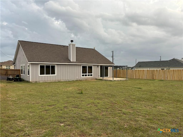rear view of house featuring a chimney, fence, a yard, and a patio