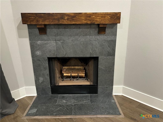 interior details featuring baseboards, a tiled fireplace, and wood finished floors