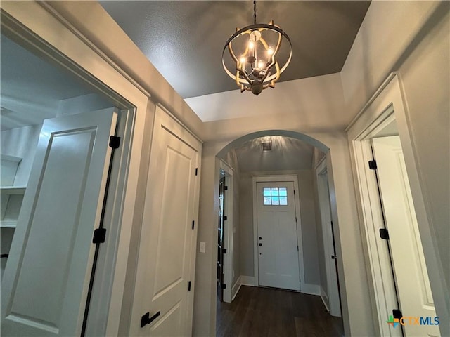 entryway featuring arched walkways, baseboards, dark wood-type flooring, and a notable chandelier