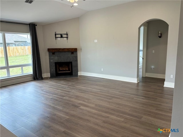 unfurnished living room with dark wood-style floors, baseboards, arched walkways, vaulted ceiling, and a ceiling fan