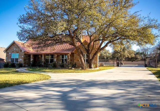 view of front of home featuring metal roof, stone siding, concrete driveway, a gate, and a front yard