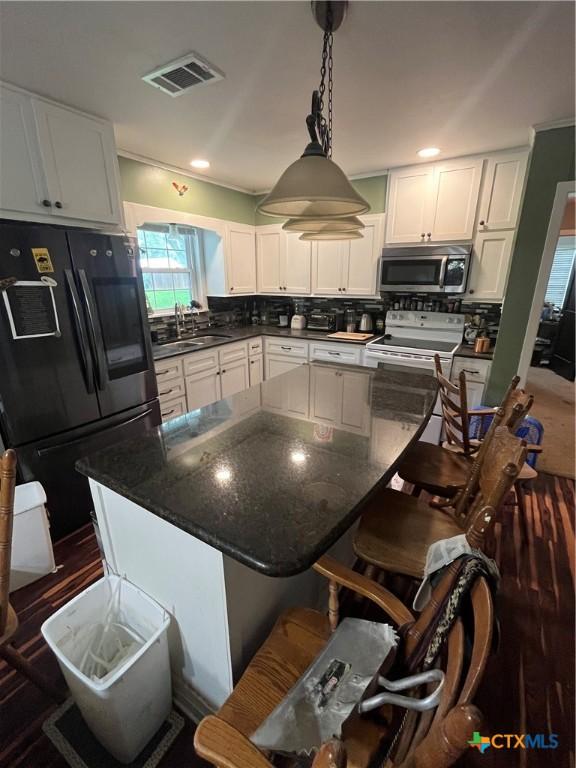 306 Angus St, Victoria, TX 77904 - kitchen featuring freestanding refrigerator, stainless steel microwave, white electric stove, white cabinets, and backsplash