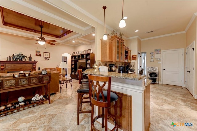kitchen featuring glass insert cabinets, light stone counters, ornamental molding, and a ceiling fan