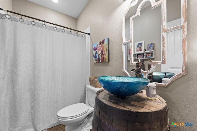 full bath featuring a shower with shower curtain, toilet, vanity, and a textured wall