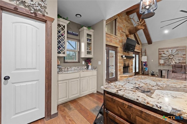 kitchen featuring light wood-type flooring, light stone counters, a fireplace, glass insert cabinets, and vaulted ceiling with beams