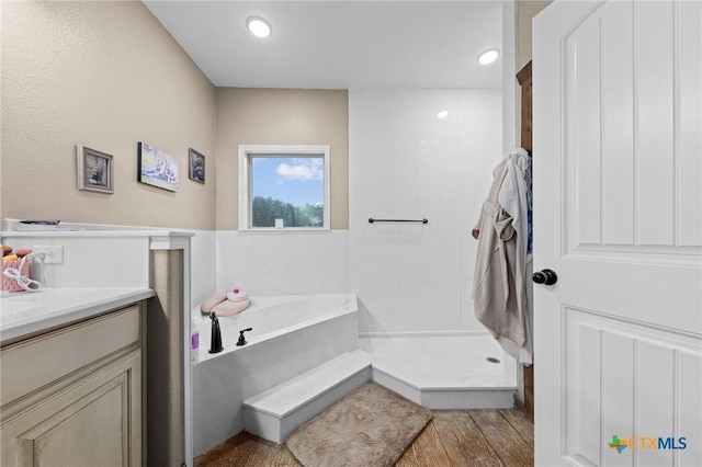 bathroom with a garden tub, wood finished floors, recessed lighting, walk in shower, and vanity