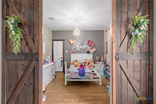 bedroom featuring visible vents, a barn door, an inviting chandelier, and wood finished floors