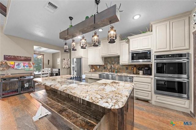 kitchen featuring visible vents, a sink, decorative backsplash, stainless steel appliances, and wood-type flooring