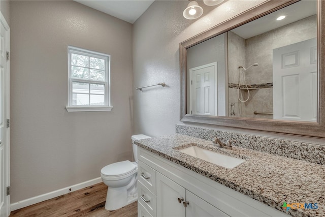 bathroom featuring hardwood / wood-style floors, vanity, toilet, and tiled shower