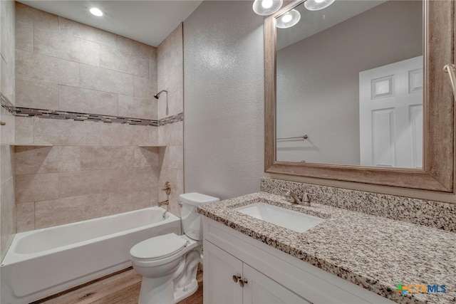 full bathroom featuring hardwood / wood-style flooring, tiled shower / bath combo, toilet, and vanity