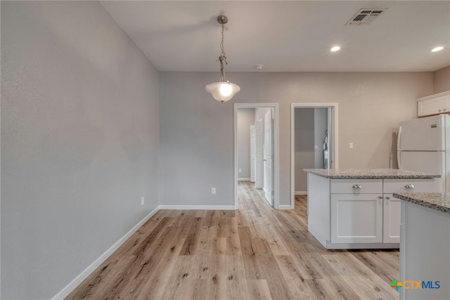 1408 Armstrong St, Luling, TX 78648 - kitchen with freestanding refrigerator, light wood-style floors, white cabinets, hanging light fixtures, and light stone counters
