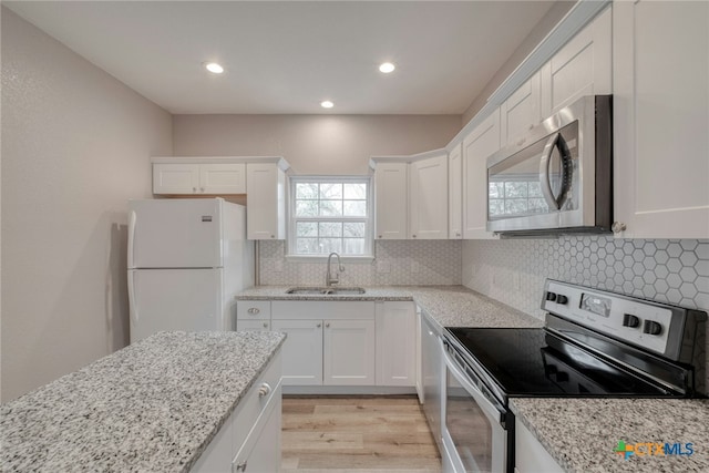 kitchen with backsplash, white cabinets, sink, light hardwood / wood-style flooring, and appliances with stainless steel finishes