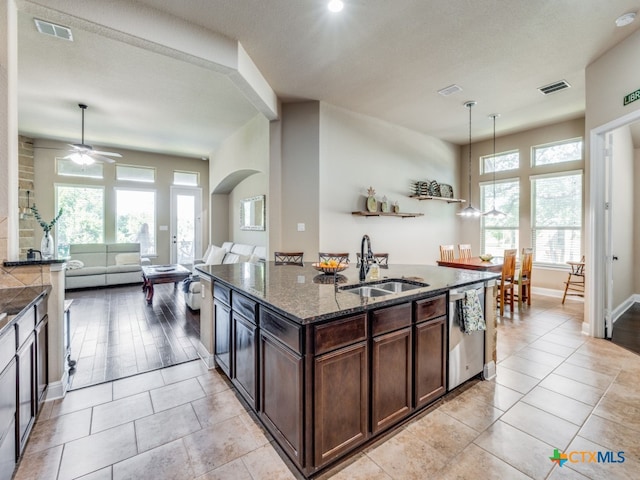 kitchen with a healthy amount of sunlight, stainless steel dishwasher, sink, and dark stone countertops