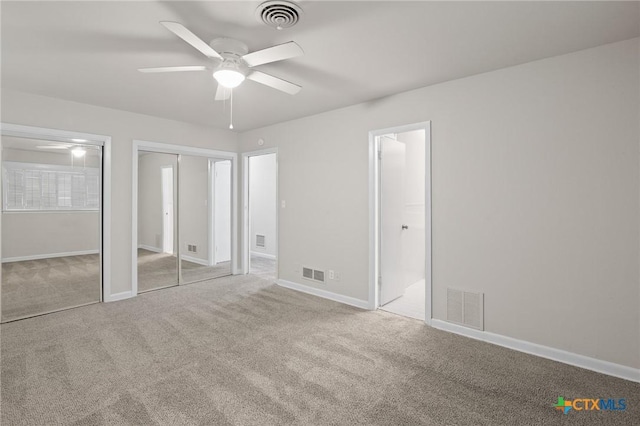 unfurnished bedroom featuring multiple closets, ensuite bath, and light carpet