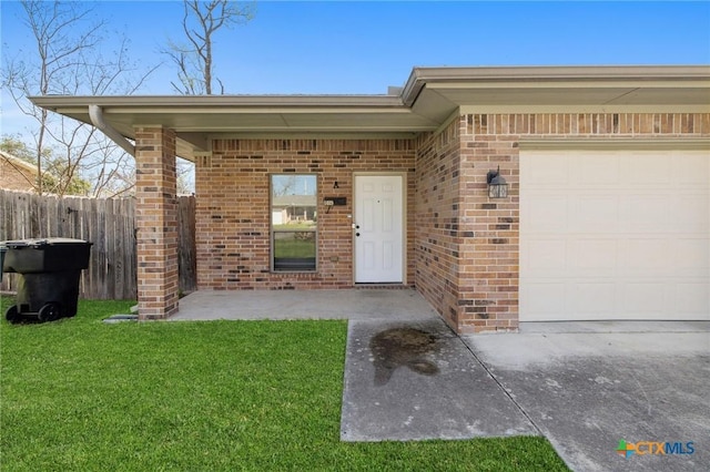 property entrance featuring brick siding, an attached garage, a yard, and fence