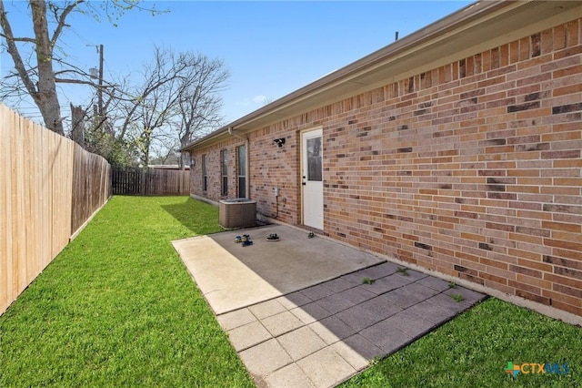 doorway to property featuring fence, a yard, cooling unit, brick siding, and a patio area