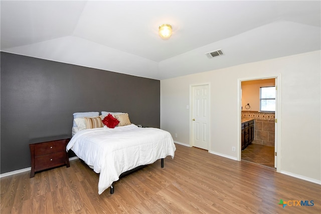 bedroom featuring ensuite bathroom, hardwood / wood-style floors, and lofted ceiling