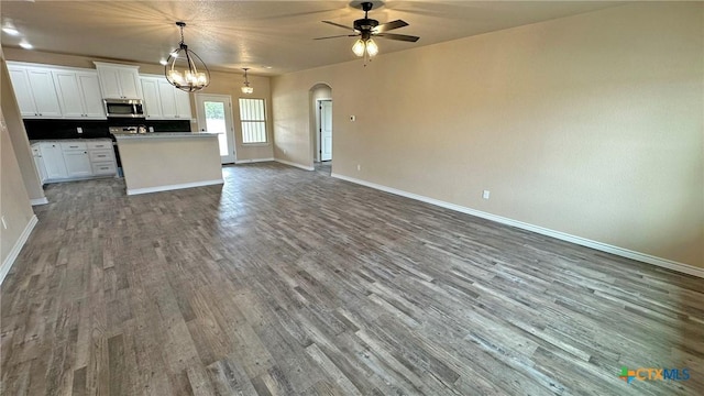 kitchen featuring dark wood finished floors, open floor plan, stainless steel microwave, ceiling fan with notable chandelier, and white cabinets