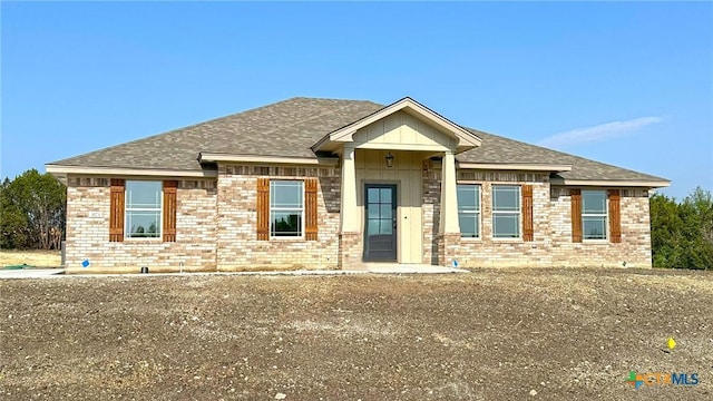 view of front of property featuring brick siding and roof with shingles