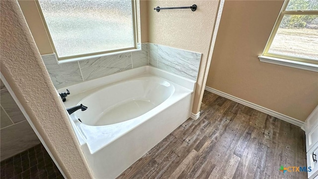 full bath with a garden tub, baseboards, wood finished floors, and a healthy amount of sunlight