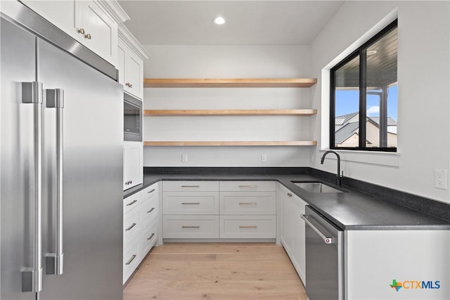 kitchen with dark countertops, appliances with stainless steel finishes, open shelves, and a sink
