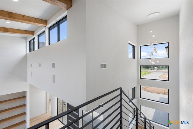 stairway featuring a high ceiling, a notable chandelier, beam ceiling, and visible vents