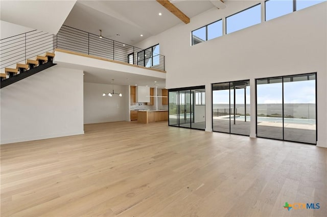 unfurnished living room with baseboards, light wood-style flooring, a towering ceiling, and stairs
