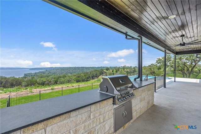view of patio / terrace featuring a grill, exterior kitchen, fence, ceiling fan, and a view of trees