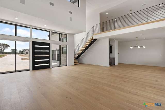 unfurnished living room with stairway, wood finished floors, a towering ceiling, and visible vents