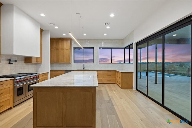 kitchen featuring range with two ovens, a center island, a sink, and light wood-style floors