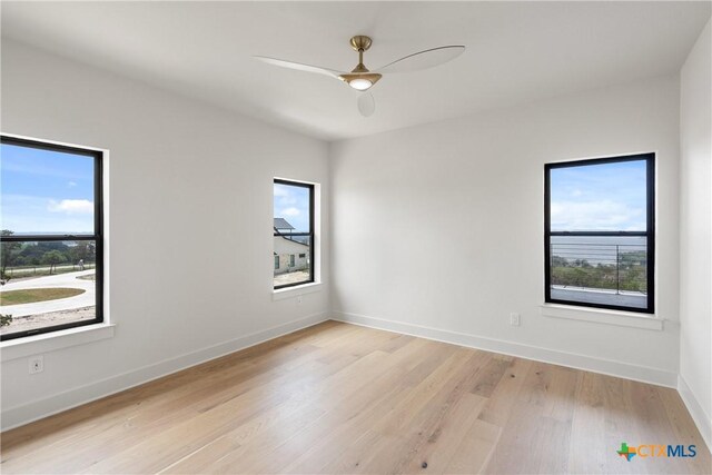 spare room with baseboards, a wealth of natural light, a ceiling fan, and light wood-style flooring