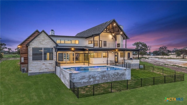 rear view of house featuring a jacuzzi, a fenced backyard, a standing seam roof, stone siding, and a lawn