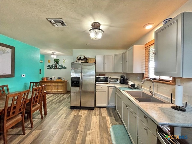 kitchen with sink, light hardwood / wood-style flooring, gray cabinets, appliances with stainless steel finishes, and a textured ceiling