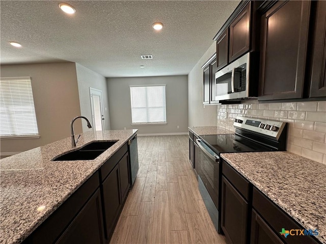 kitchen featuring backsplash, sink, light stone counters, dark brown cabinetry, and stainless steel appliances