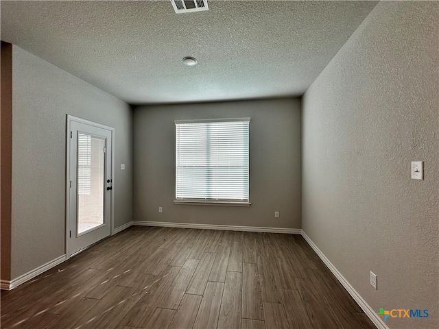 spare room with dark hardwood / wood-style flooring, a textured ceiling, and a wealth of natural light