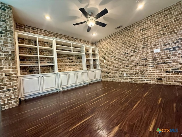 empty room featuring dark hardwood / wood-style floors, ceiling fan, and brick wall