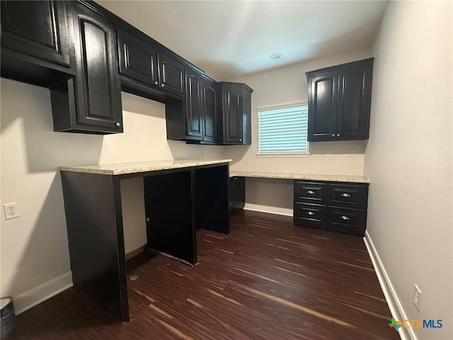 kitchen featuring light stone countertops, built in desk, and dark wood-type flooring