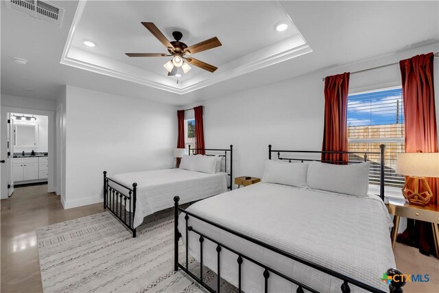 bedroom featuring crown molding, ceiling fan, ensuite bathroom, and a tray ceiling