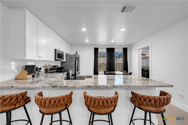 kitchen with white cabinetry, appliances with stainless steel finishes, a kitchen breakfast bar, kitchen peninsula, and light stone countertops