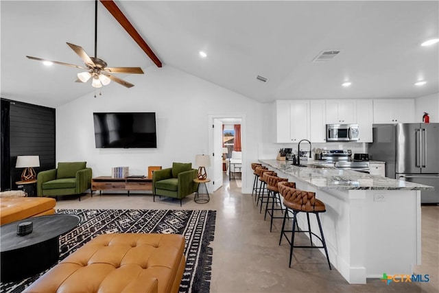 kitchen with white cabinetry, vaulted ceiling with beams, light stone counters, kitchen peninsula, and stainless steel appliances