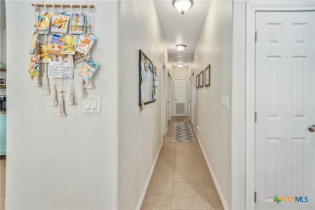 hall featuring attic access, light tile patterned flooring, and baseboards