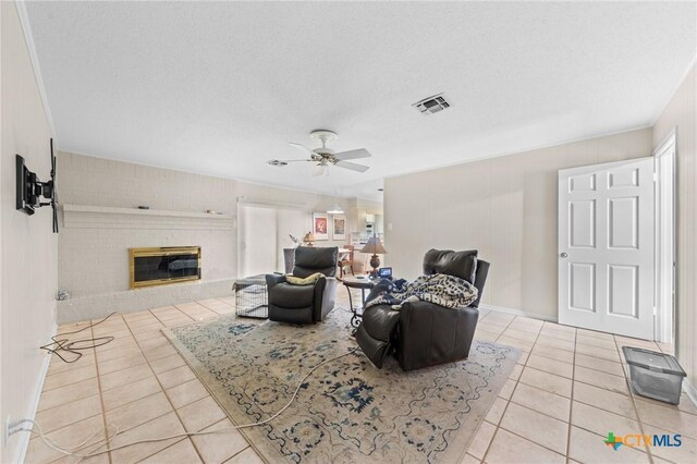 tiled living area featuring a brick fireplace, ceiling fan, and visible vents