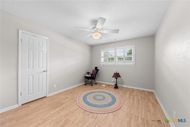 misc room with a textured ceiling, baseboards, a ceiling fan, and wood finished floors