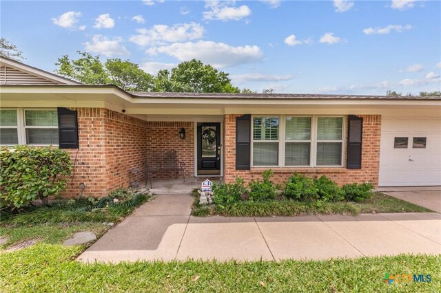 entrance to property featuring brick siding, an attached garage, and driveway