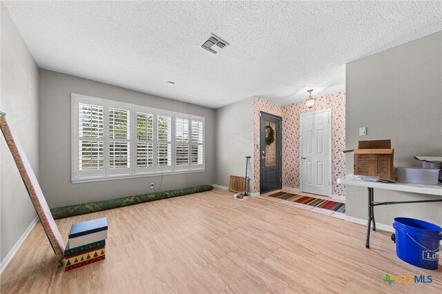 entrance foyer featuring baseboards, a textured ceiling, wood finished floors, and visible vents