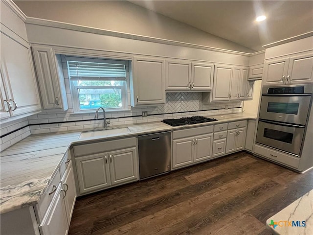 kitchen featuring appliances with stainless steel finishes, vaulted ceiling, white cabinets, and a sink