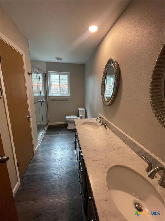 bathroom featuring visible vents, a sink, toilet, and a shower stall