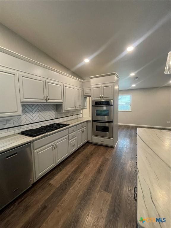 kitchen featuring dark wood-style flooring, white cabinets, vaulted ceiling, appliances with stainless steel finishes, and decorative backsplash