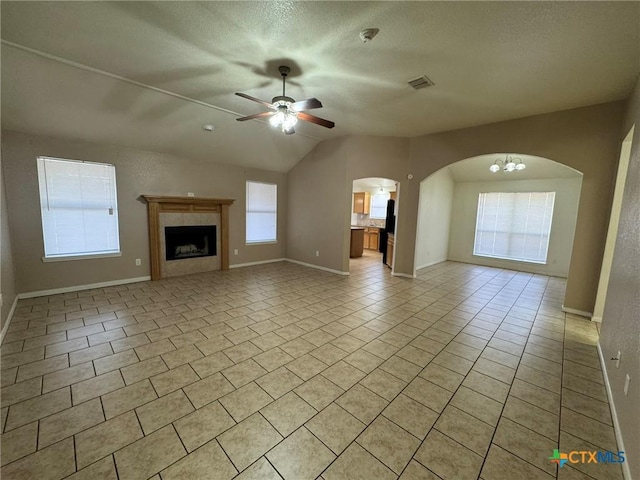 unfurnished living room featuring vaulted ceiling, a textured ceiling, light tile patterned floors, a tiled fireplace, and ceiling fan with notable chandelier